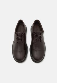 Scarpe in pelle marrone con una texture liscia, design con lacci, punta rotonda e stile minimalista. Suola in gomma con bordi arrotondati.