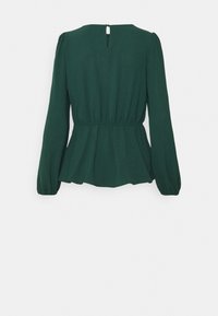 Blouse vert foncé avec de longues manches bouffantes, taille froncée et détail de dos en trou de serrure. Tissu doux avec une texture lisse.