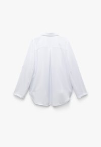 Camisa blanca de manga larga con cuello, dobladillo curvado y un pliegue en la parte posterior. Textura suave y puños con botones, con un diseño minimalista.
