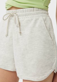 Shorts de sport gris clair avec une taille élastique, fermeture à cordon et poches latérales ; texture douce et coupe décontractée.