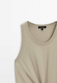 Débardeur beige sans manches avec encolure ronde et coutures visibles autour des bords sur un fond blanc.