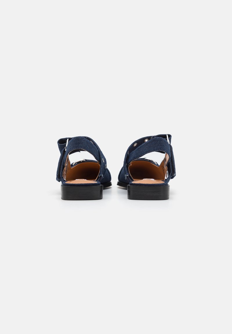Dunkelblaue Wildledersandalen mit flacher schwarzer Sohle, offenem Absatz und verstellbarem Knöchelriemen mit silberner Hardware. Schlichtes Design mit glatter Textur.