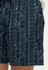 Σκούρο μπλε σορτς με μεγάλο λευκό λογότυπο σε επαναλαμβανόμενο μοτίβο. Διαθέτει κορδόνι στη μέση και μαλακό, ελαφρύ ύφασμα.