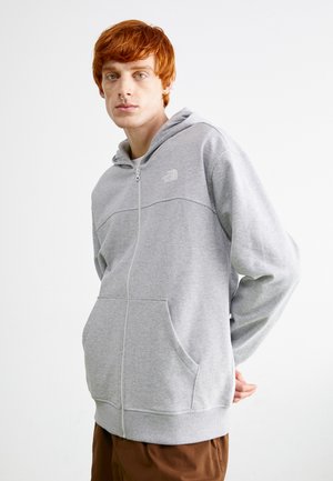 Haut à zip gris clair fabriqué en tissu doux, doté d'une poche kangourou, de poignets côtelés et d'un petit logo sur la poitrine.