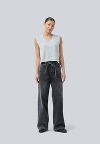 Light gray sleeveless knit top with a v-neck, paired with high-waisted dark gray wide-leg jeans featuring a tied waist detail.