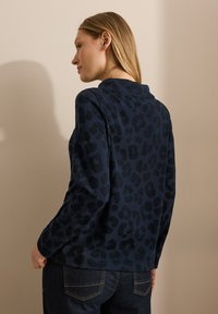 Haut à manches longues marine avec un motif léopard noir discret. Tissu lisse avec un ourlet arrondi et une coupe décontractée.