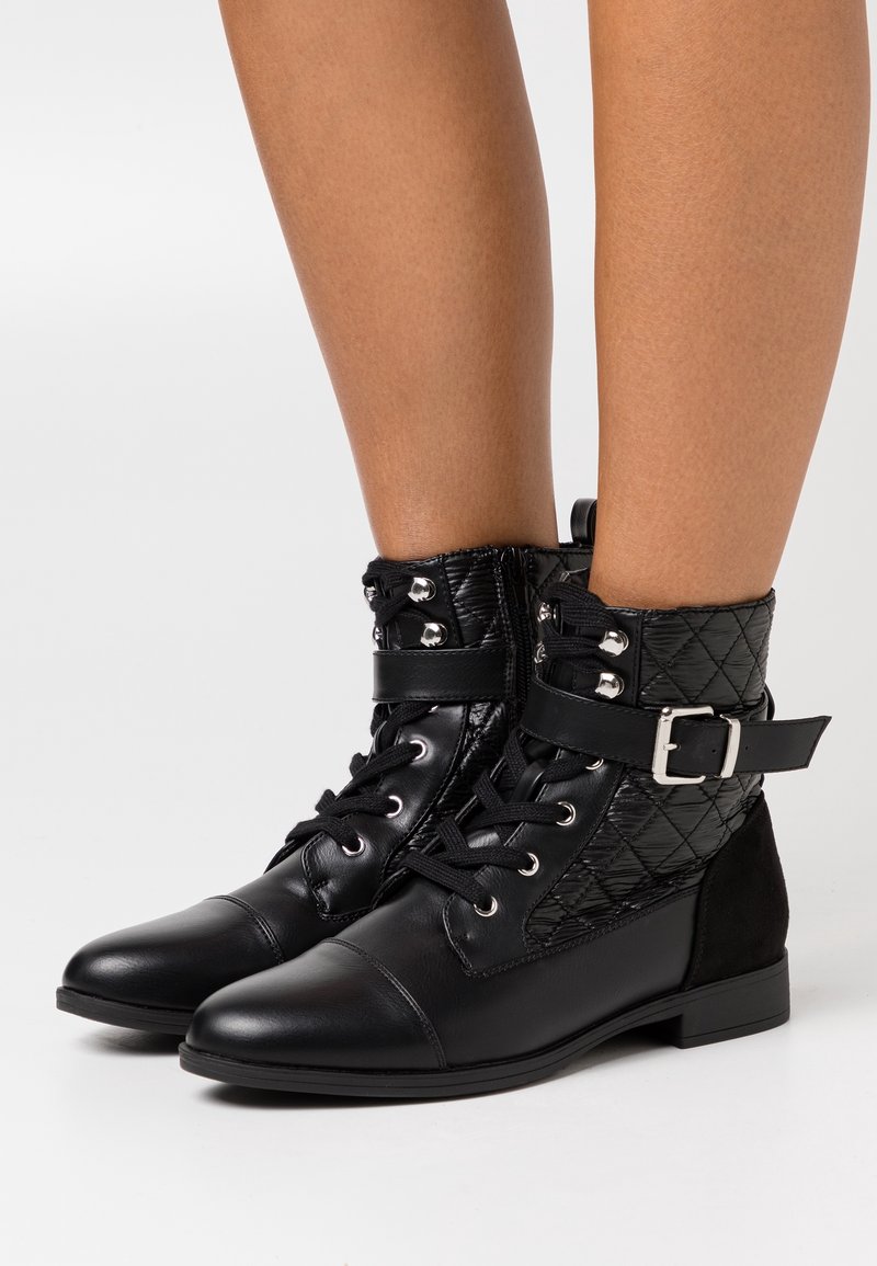 Botines negros hasta el tobillo con un upper de cuero acolchado, que presentan una correa con hebilla, cordones en la parte delantera y un tacón plano. Punta lisa y acabado mate.
