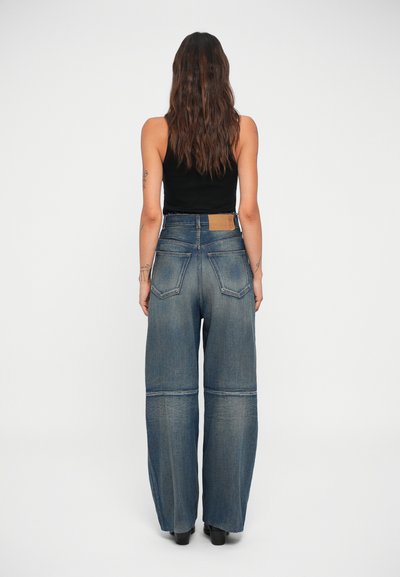 Wide-leg denim jeans in mid-blue, featuring a high waist, two back pockets, and stitching details. Smooth texture with slight fade.