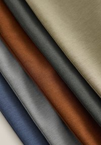 Viisi taitettua kangaspalaa maalaisten sävyissä: beige, oliivi, ruoste, liuskekiviväri ja laivastonsininen. Värikäs, pehmeä materiaali hienolla neulekuviolla.