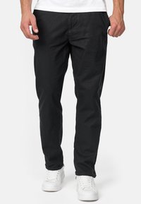 Fekete szövet nadrág slim fit szabásban, oldalsó zsebekkel és egyenes lábbal, fehér sportcipővel párosítva.