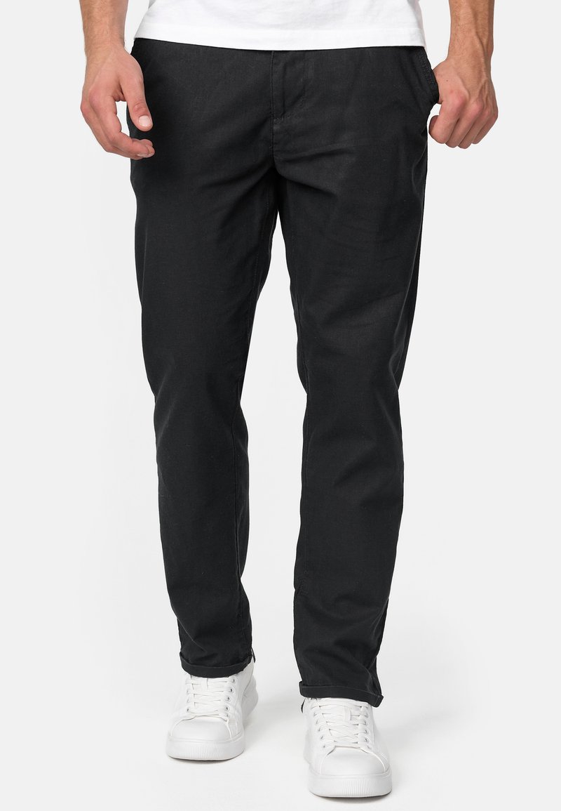 Fekete szövet nadrág slim fit szabásban, oldalsó zsebekkel és egyenes lábbal, fehér sportcipővel párosítva.