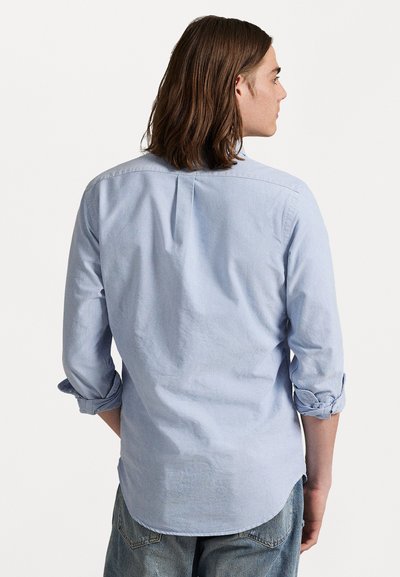 Lichtblauw overhemd met lange mouwen, opgerold bij de manchetten, ontspannen pasvorm en een rugplooi; gedragen over casual denim jeans.