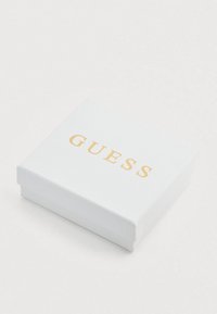Weißer, strukturiert Box mit einem goldenen "GUESS"-Logo auf der Oberseite. Quadratische Form, minimalistisches Design, glatte Kanten. Eignet sich für Schmuck oder kleine Gegenstände.