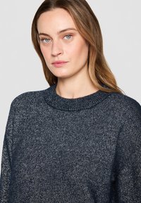 Maglione in maglia blu navy con scollatura rotonda e maniche lunghe. Il materiale presenta una superficie testurizzata con effetto metallico. Vestibilità regolare.