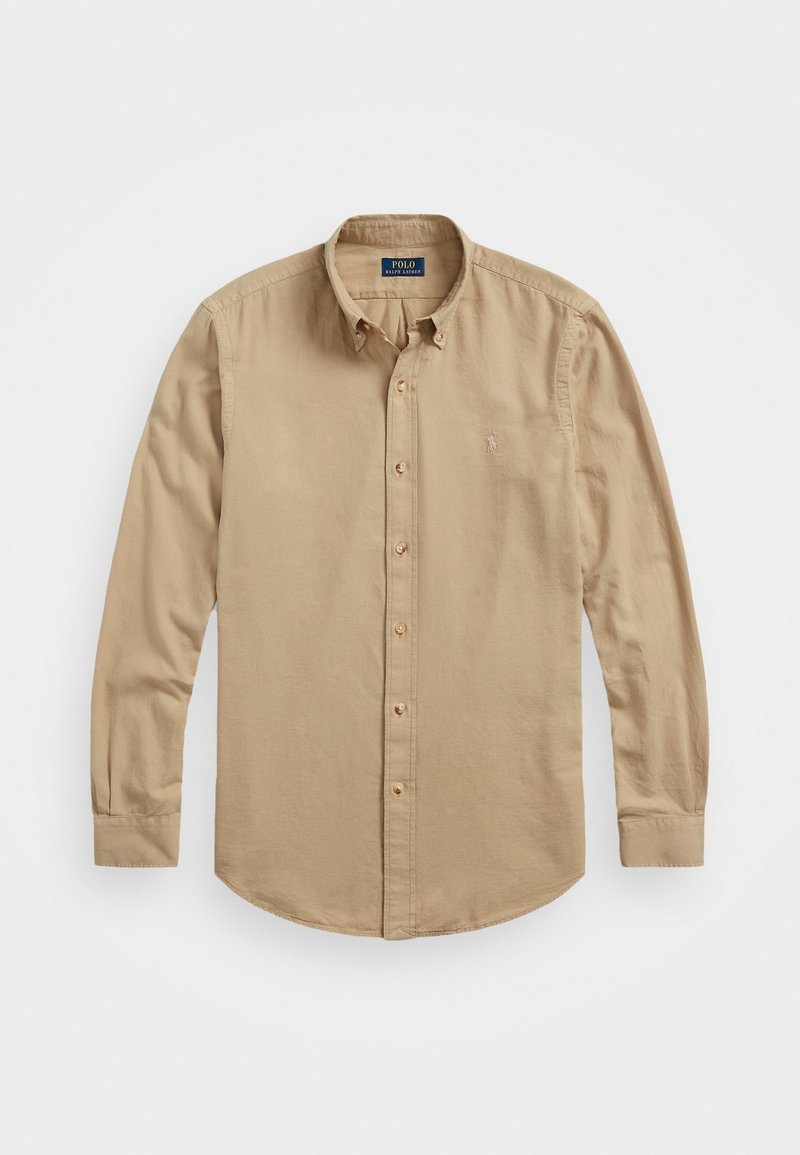 Chemise beige à manches longues avec boutons, col, manches à revers et logo brodé subtil sur la poitrine gauche.