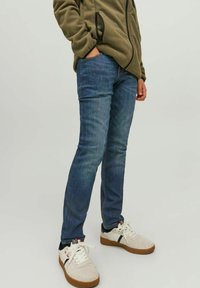 Blå denimjeans med slim fit, femfickorsdesign och ljus blekning. Kombinerade med en grön fleecejacka och vita sneakers.