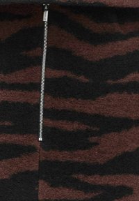 Brun och svart tigerstrimmig tyg med en slät yta har en silverfärgad metalldragkedja i mitten.