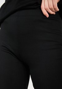 Leggings noires à côtes avec une taille haute, présentant un motif texturé et un design ajusté, vues d'un angle rapproché.