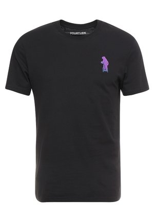 T-shirt noir à manches courtes avec un petit ours violet brodé en train de conduire une trottinette bleue sur le côté gauche de la poitrine.