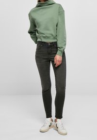 Sudadera de algodón verde claro con cuello alto, combinada con jeans ajustados gris oscuro y zapatillas blancas con detalles verdes.