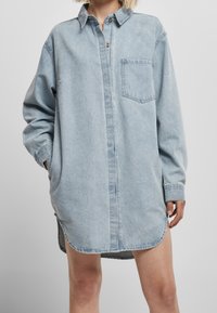 Denim-kjole i lyseblå med knaplukning foran, brystlomme, lange ærmer og buet kant; har en afslappet, oversized pasform.