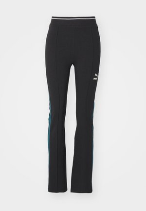 Pantalons noirs évasés avec des rayures latérales en teal contrasté. La taille élastique présente un accent blanc. Le matériau semble extensible et lisse.