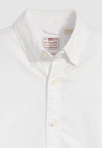 Cămașă albă cu nasturi, realizată din bumbac, cu guler ascuțit. Prezintă nasturi de culoare crem și o etichetă cu marca Levi's pe interior.