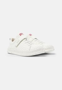 Sneakers bianchi con texture perforata, dotati di una fascia in velcro e chiusura con lacci. Accentuati da una leggera spruzzata sulla suola. Marchio rosso visibile.