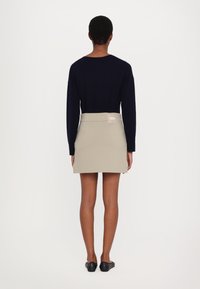 Marineblå langermet topp og beige tettsittende skjørt med en synlig logo på livet, båret med sorte flats. Glatt stoff og skreddersydd design.