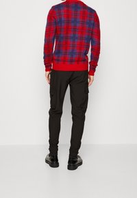 Rot-blau karierter Pullover mit langen Ärmeln und gerippten Bündchen, kombiniert mit schwarzen Cargo-Hosen mit seitlichen Taschen und schmalem Schnitt.