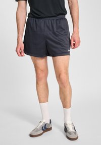 Svarta träningsshorts med nättextur, elastisk midja och logotyp. Bärs med grå och marinblå sneakers och vita ankelsockor.