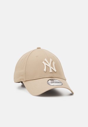 Beżowa regulowana czapka z daszkiem z białym haftowanym logo New York Yankees na przodzie i zakrzywionym daszkiem.