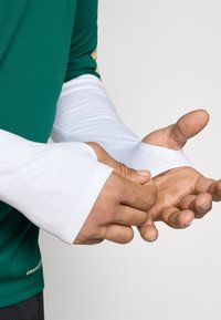 Λευκά μανίκια από ελα�φρύ ύφασμα, με υφή και εφαρμοστή σχεδίαση, φορεμένα πάνω από ένα πράσινο ρούχο.