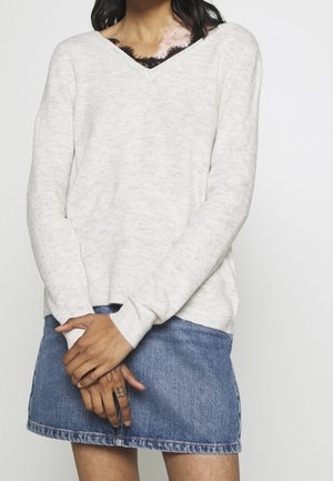 Pull en tricot gris clair avec un col en V, associé à une mini-jupe en denim. Il est doté de manches longues et d'une coupe décontractée.