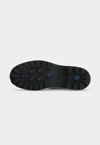 Semelle de chaussure noire avec des crampons profonds et six inserts circulaires bleus, affichant la marque Geox et un design respirant breveté.