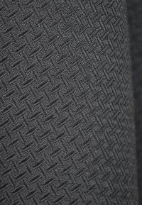 Teksturowana czarna tkanina z tkanym wzorem w jodełkę, o gęstej, matowej powierzchni i równomiernym szyciu.