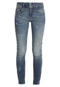 Vaqueros ajustados en denim azul desteñido, con detalles desgastados y un diseño clásico de cinco bolsillos. Cintura con pasadores para cinturón y cierre de botón.