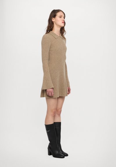 Rochie tricotată bej cu mâneci lungi evazate și guler clasic, asortată cu cizme din piele neagră până la genunchi, cu toc pătrat.