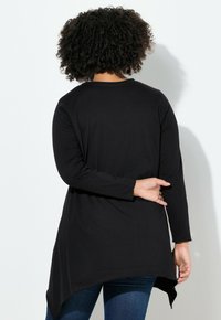 Tunique noire à manches longues avec un ourlet arrondi, fabriquée en tissu lisse. Présente une coupe décontractée et un subtil détail de couture au niveau du col.