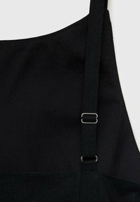 Tablier en tissu noir avec une sangle ajustable comportant une boucle métallique et un anneau sur un fond clair.