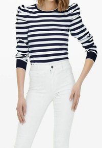 Maglietta a righe navy e bianca a maniche lunghe con spalle gonfie e polsini a costine, abbinata a pantaloni bianchi aderenti.