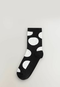 Czarne skarpetki z dużymi białymi kropkami; dzianinowy materiał; ściągacz w kostce; długość do połowy łydki; miękka tekstura; casualowy styl.