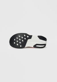 Semelle d'une chaussure de sport blanche avec une grippe en caoutchouc noir présentant un motif triangulaire et une texture de bande de roulement sur un fond uni.