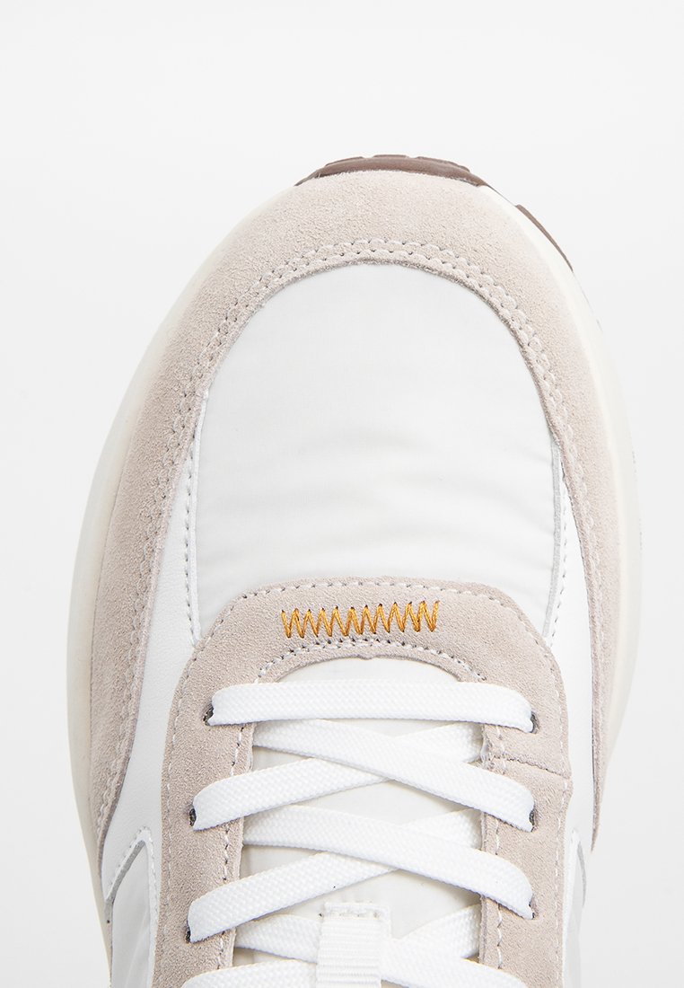 Weiße Sneakers mit beigen Wildlederakzenten, strukturiertem Obermaterial und weißen Schnürsenkeln. Verfügt über ein gesticktes Muster und eine runde Gummisohle.