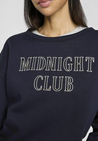 Sudadera azul marino con el texto bordado en crema "MIDNIGHT CLUB", con un escote relajado y una textura suave de algodón.