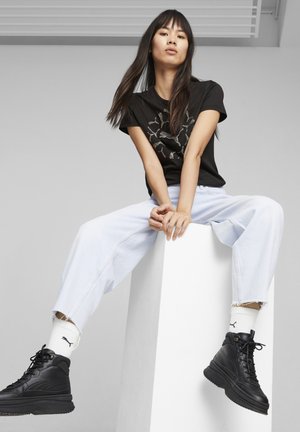 Black graphic t-shirt with white design, light blue wide-leg jeans, and black high-top sneakers. White socks with logo visible.
