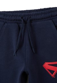 Pantalones de chándal de algodón azul marino con cintura elástica, cordón y un prominente logo rojo en forma de "S" en la parte frontal.
