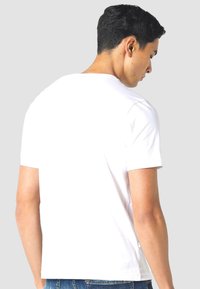 White cotton t-shirt with a crew neck and short sleeves, featuring a plain back and relaxed fit, paired with blue denim jeans.