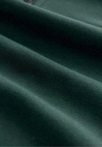 Tissu vert foncé avec une texture fine côtelée et des plis doux créant des ombres et des reflets délicats.