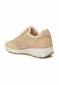 Zapatilla de color beige claro con detalles de malla tejida, acentos texturizados y una suela de plataforma blanca. Presenta tachuelas decorativas en el talón.